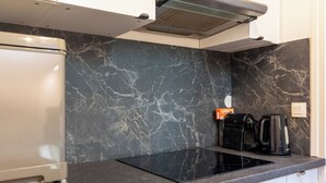 A kitchen with a black marble backsplash, a built-in stove, a coffee maker, and a refrigerator.