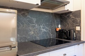 A kitchen with a black marble backsplash, a built-in stove, a coffee maker, and a refrigerator.