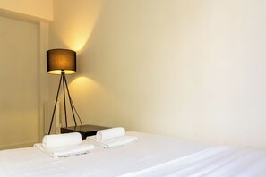 A hotel room with a bed, a nightstand, a lamp, and two rolled towels.