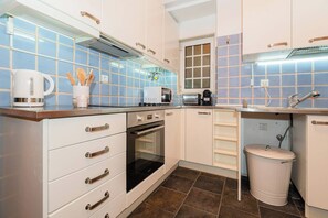 A kitchen with white cabinets, a stove, a microwave, and a trash can.
