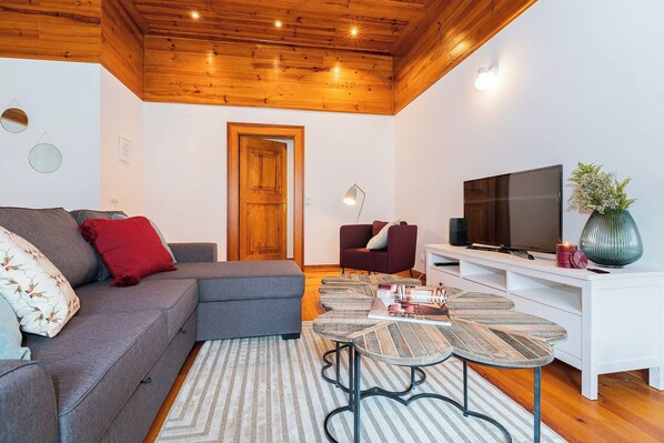 A modern living room with a sectional sofa, a TV, a coffee table, and a wooden ceiling.
