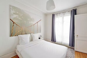 A bedroom with a bed, a wall-mounted artwork, a window with curtains, and a door. - Cosy flat for 2 people near Pigalle (Paris)