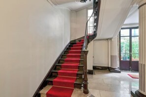 A staircase with red carpeted steps and a wooden handrail, leading to a door with a white frame. - Cosy flat for 2 people near Pigalle (Paris)