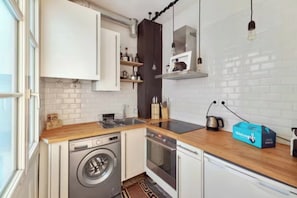 A compact kitchen with a washing machine, oven, and a coffee maker. - Cosy flat for 2 people near Pigalle (Paris)