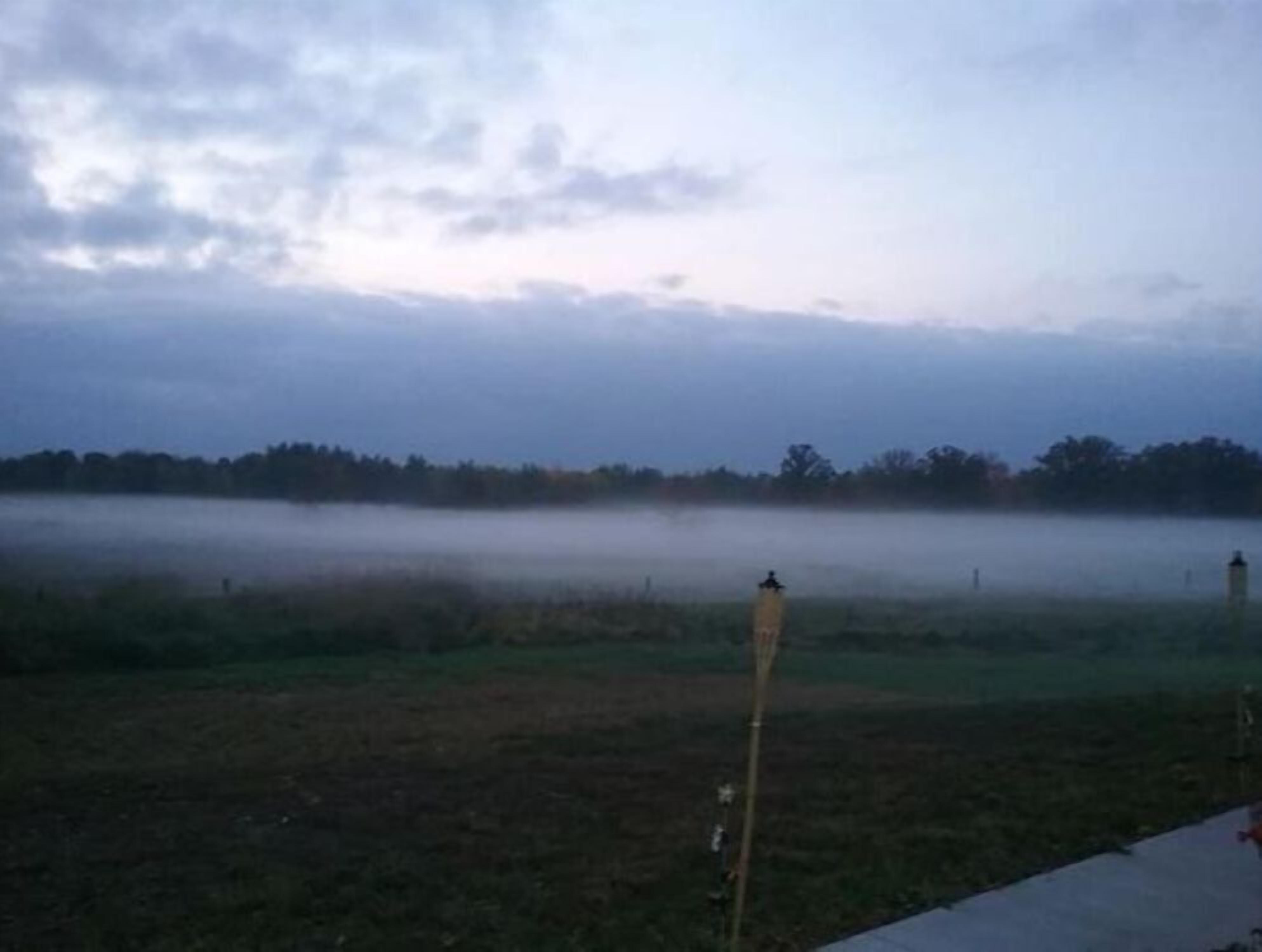 A misty field with a fence and a person standing in the distance.