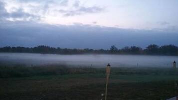 A misty field with a fence and a person standing in the distance.