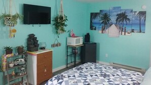 Una stanza con pareti color verde acqua, un letto con copriletto decorato, una TV fissata al muro e un quadro a tema spiaggia.
