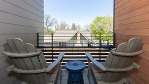 Un balcon agrémenté de deux fauteuils Adirondack et d’une petite table ronde, donnant sur un quartier résidentiel avec des arbres et une maison.