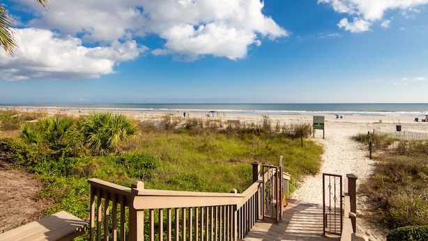 A beach pathway leading to the ocean with a wooden railing and a sign.