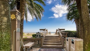 A wooden staircase leading to a beach, with palm trees and a clear sky.