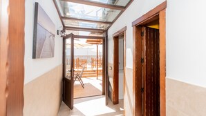 Un pasillo con tragaluces que da a un espacio exterior con terraza de madera y sillas.