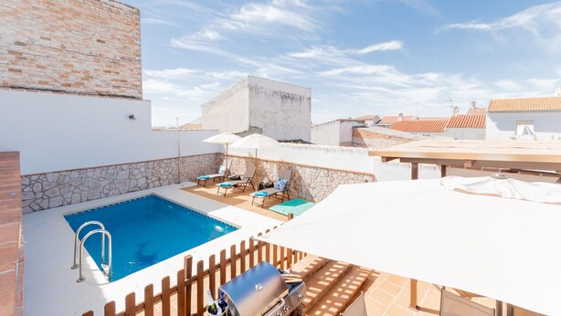 Una piscina en la azotea con un muro de piedra, sillas de descanso y sombrillas.