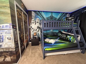Une chambre avec un lit superposé décorée de posters Star Wars, un mur sur le thème de Star Wars et une couvre-lit aux motifs Star Wars.