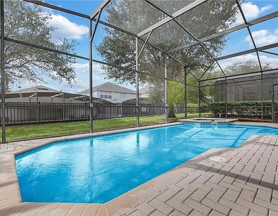 A swimming pool with a covered area, surrounded by a brick patio and a metal fence.
