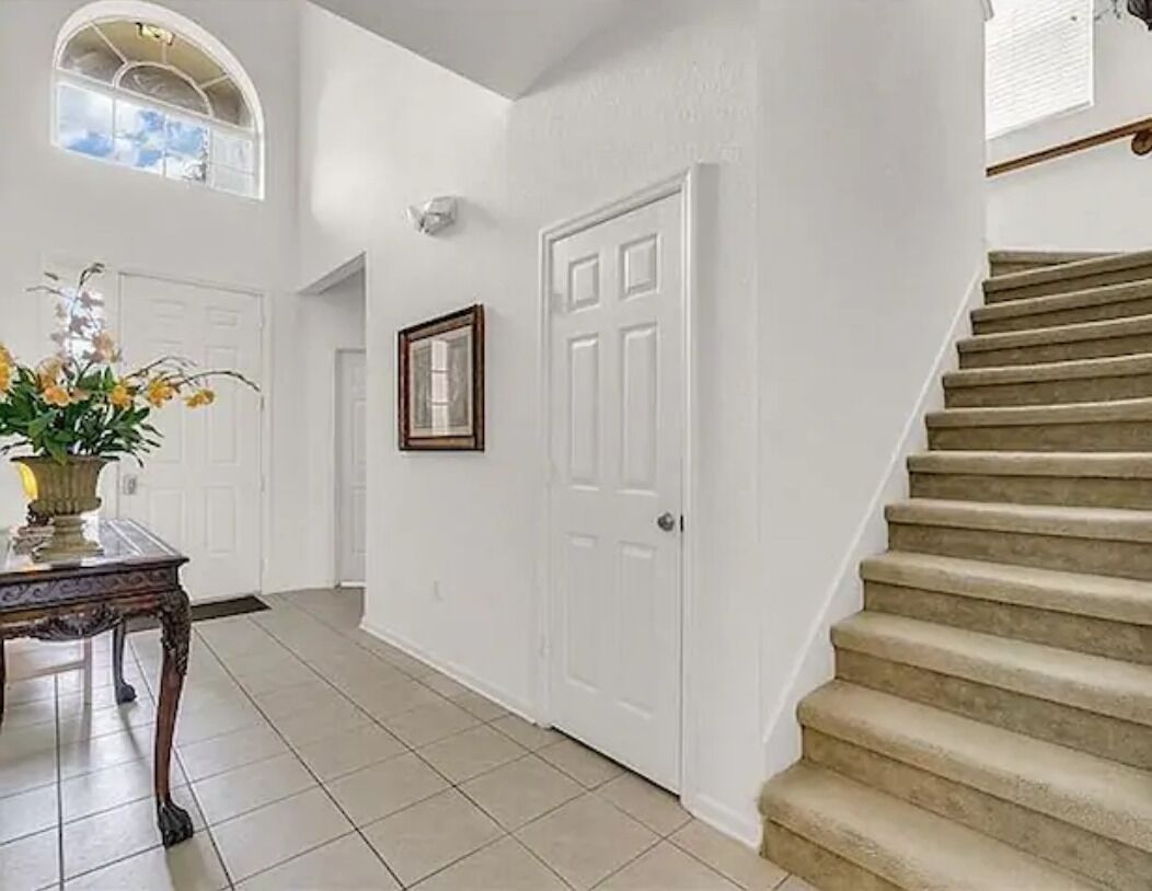 A hallway with a staircase, a white door, and a framed picture on the wall.