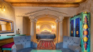 A room with a bed, two armchairs, a table with a decorative item, and a colorful cabinet. - Acer Cave Hotel (Ürgüp)