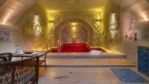 A spa room with a red bathtub, a wooden bench, and a dining area with wicker chairs. - Acer Cave Hotel (Ürgüp)