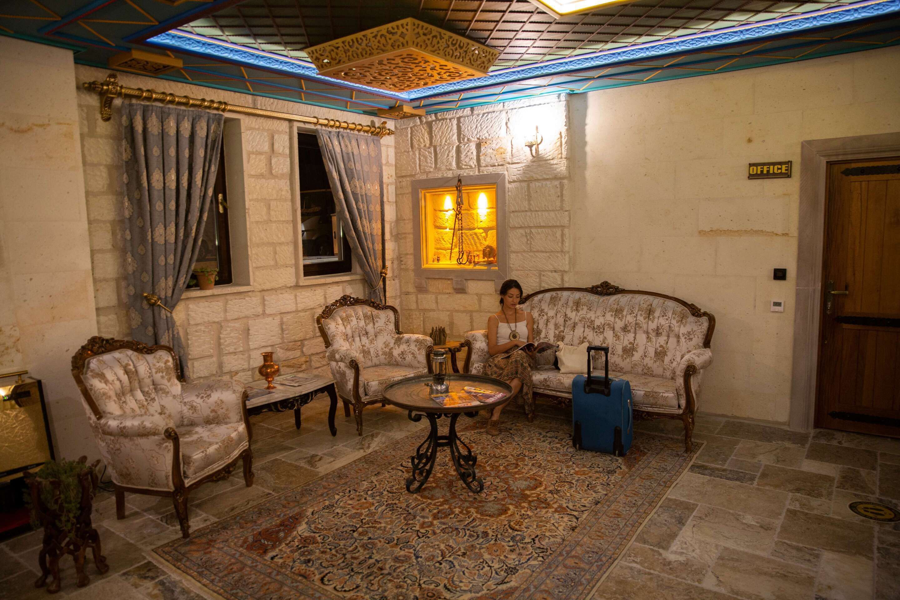 A room with a patterned rug, a sofa, two armchairs, a small table, and a window with curtains.