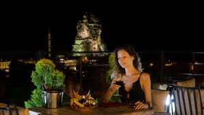A woman sitting at a wooden table with a wine glass, a metal bucket with food, and a potted plant. - Acer Cave Hotel (Ürgüp)