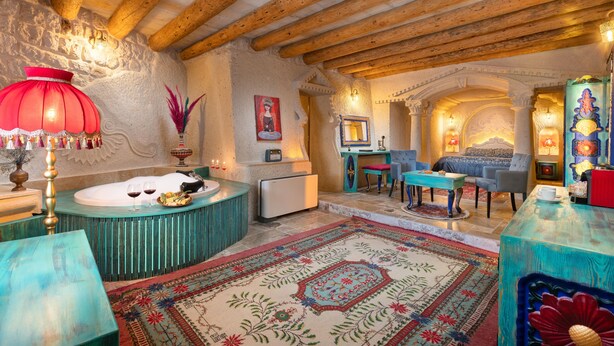 A cozy room with a wooden ceiling, a large red lamp, a bathtub, and a seating area with a blue sofa and a small table. - Acer Cave Hotel (Ürgüp)