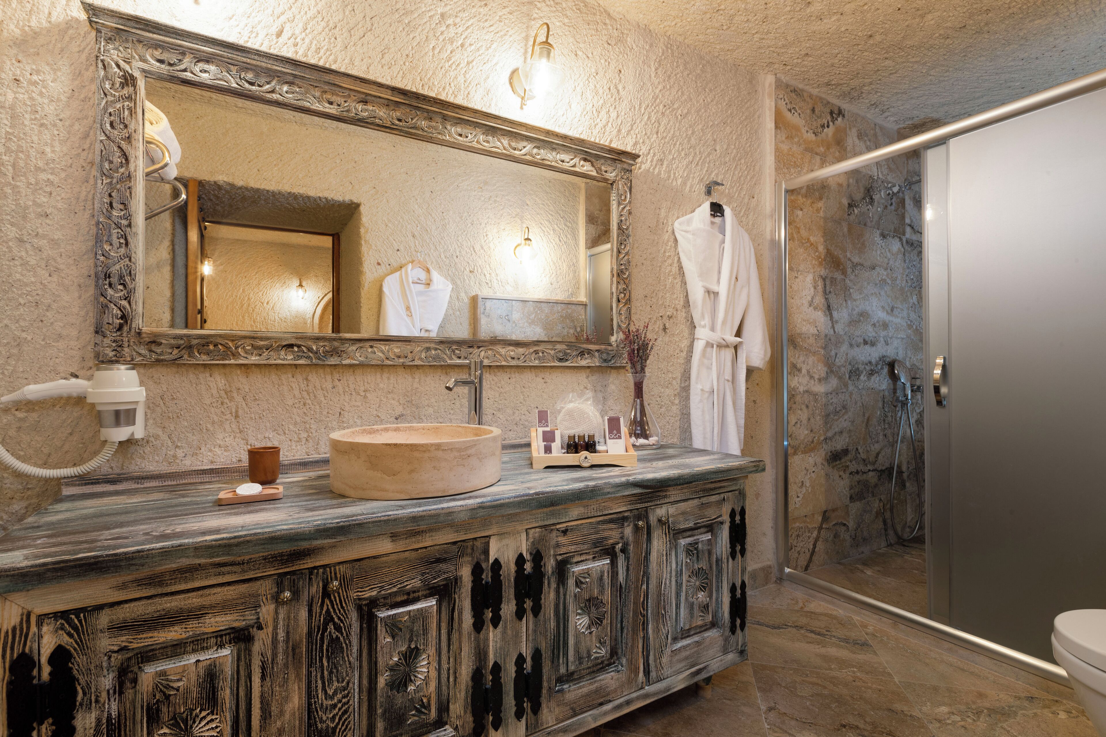 A bathroom with a large mirror, a wooden vanity, a stone sink, and a shower area.