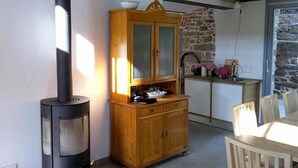 A cozy room with a wood-burning stove, a wooden cabinet, a stone wall, and a kitchen area with a sink and countertop.