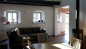 A spacious living room with a high ceiling, two windows with curtains, a sofa, a small table, and a fireplace.