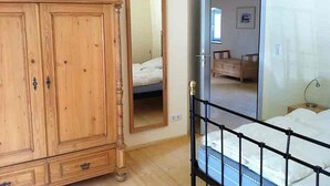 A bedroom with a wooden wardrobe, a bed with a black metal frame, and a mirror reflecting a bed and a dresser.