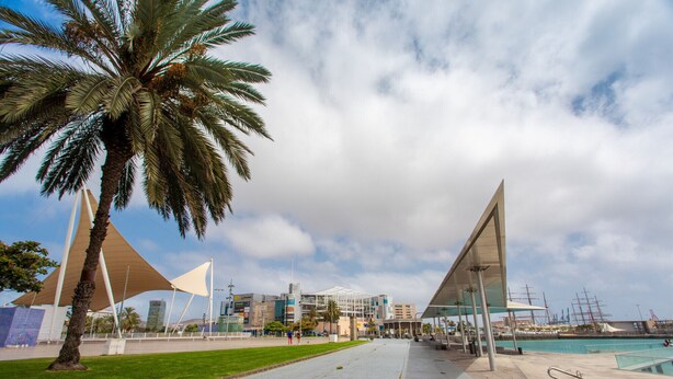 Un paseo marítimo con arquitectura moderna, que incluye una gran estructura de vidrio y una palmera.