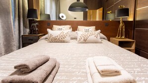 Una cama bien hecha con una colcha estampada, dos almohadas decorativas y una pila de toallas dobladas.
