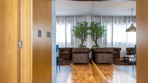 Una sala de estar moderna con piso de madera, dos sofás marrones, una mesa de centro y una planta de árbol grande.