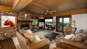 Una sala de estar acogedora con chimenea, sofás de cuero, una mesa de centro y un gran ventanal con vistas panorámicas.