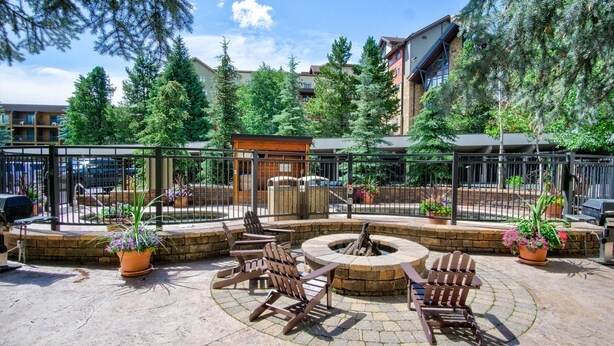 Un patio al aire libre con sillas Adirondack, un hogar para fuego y plantas en macetas.