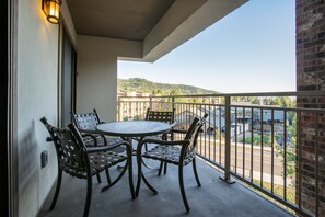 A balcony with a round table and four chairs, a light fixture, and a view of a street and buildings.