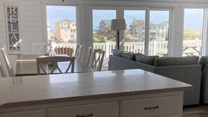 A kitchen with white cabinetry, a granite countertop, and a view of the ocean through large windows. - Perfect Ocean and Sunset Views / Deck to Sand in 2 Min (Nags Head)