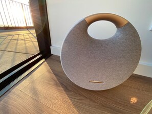 A modern, circular, textured speaker with a wooden handle, placed on a wooden floor near a glass door. - Rentals: BOUTIQUE - ATTICO Luxury Design - Ocean Views (Porto)