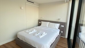 Une chambre moderne avec un grand lit, un plancher en bois et une porte-fenêtre coulissante donnant sur un balcon.