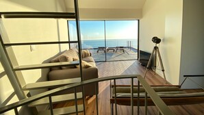 Un intérieur moderne avec un escalier menant à un balcon d’où l’on a vue sur la mer.