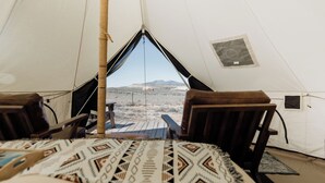 Una carpa con vista a un paisaje desértico, dos sillas de madera y una colcha estampada.