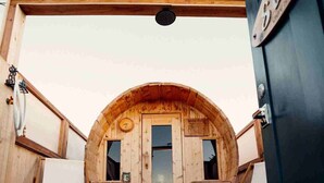 Una cabaña de madera con una entrada circular, dos sillas blancas y una terraza de madera.