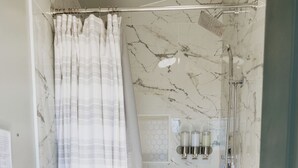 Un baño con ducha, paredes de mármol, tocador de madera y un perchero para toallas.