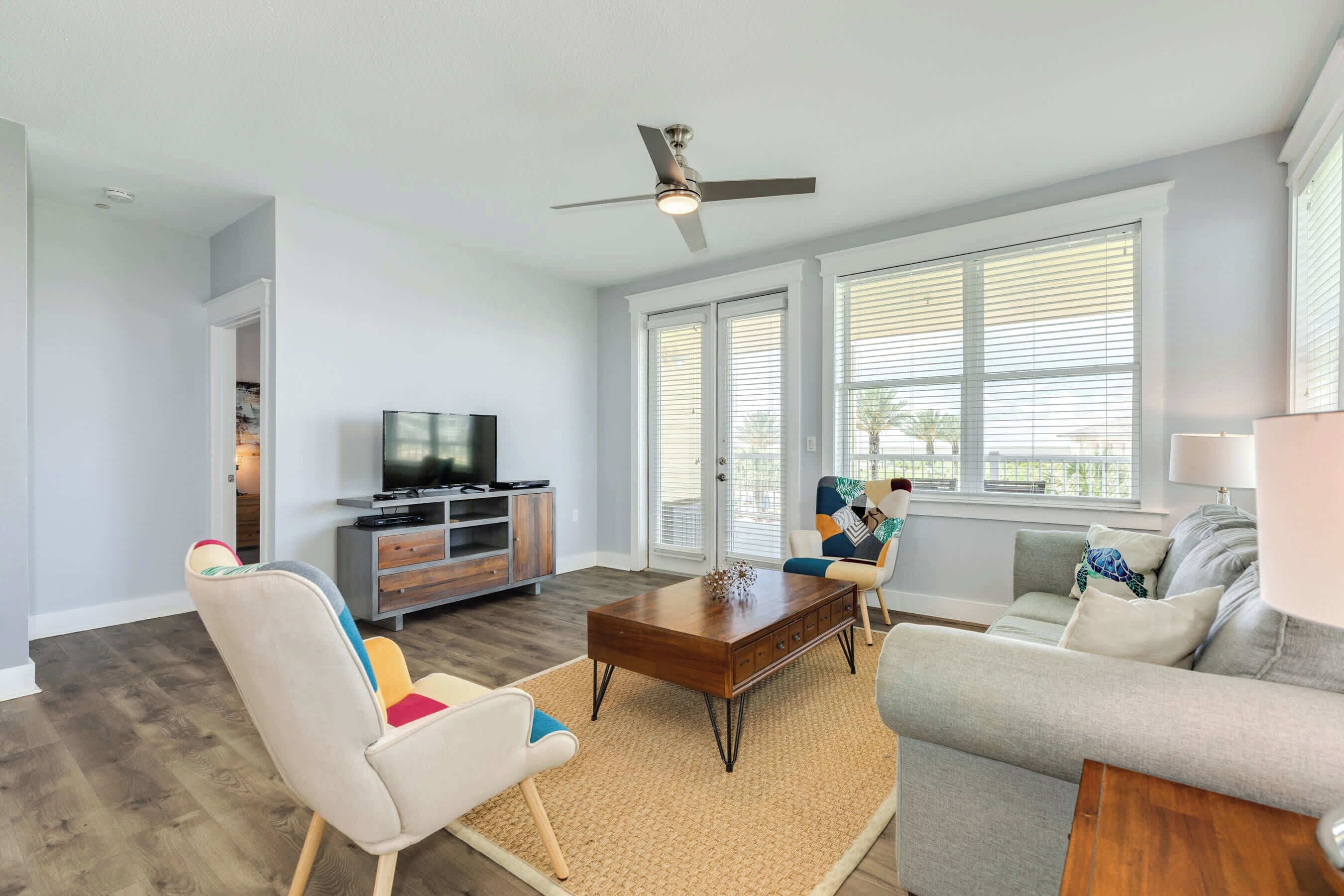 A living room with a TV, sofa, chairs, and a ceiling fan.