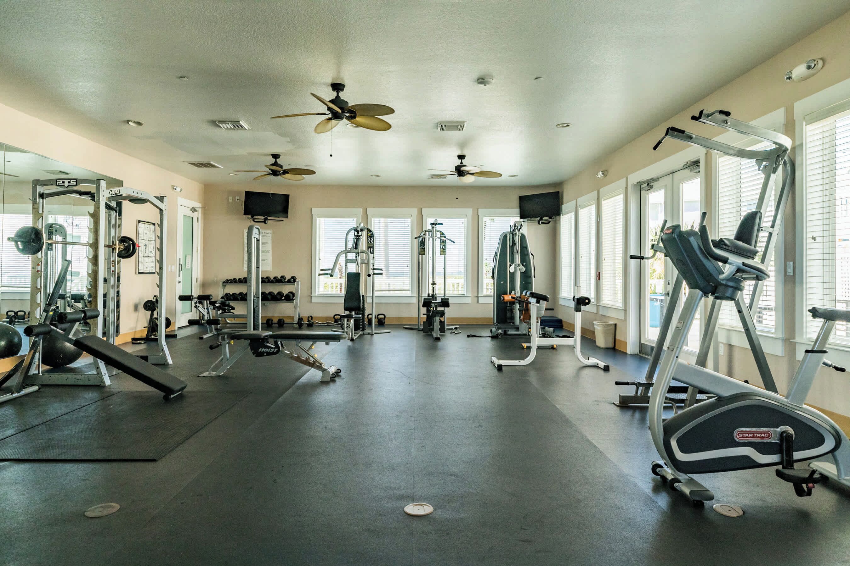 A gym with ceiling fans, various exercise equipment, and large windows.
