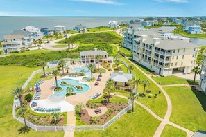 A resort with a central pool area, multiple buildings, and a view of the ocean. - Sunset Vista - Heated Pool, Lazy River, 2 x Hot Tubs! (Galveston)