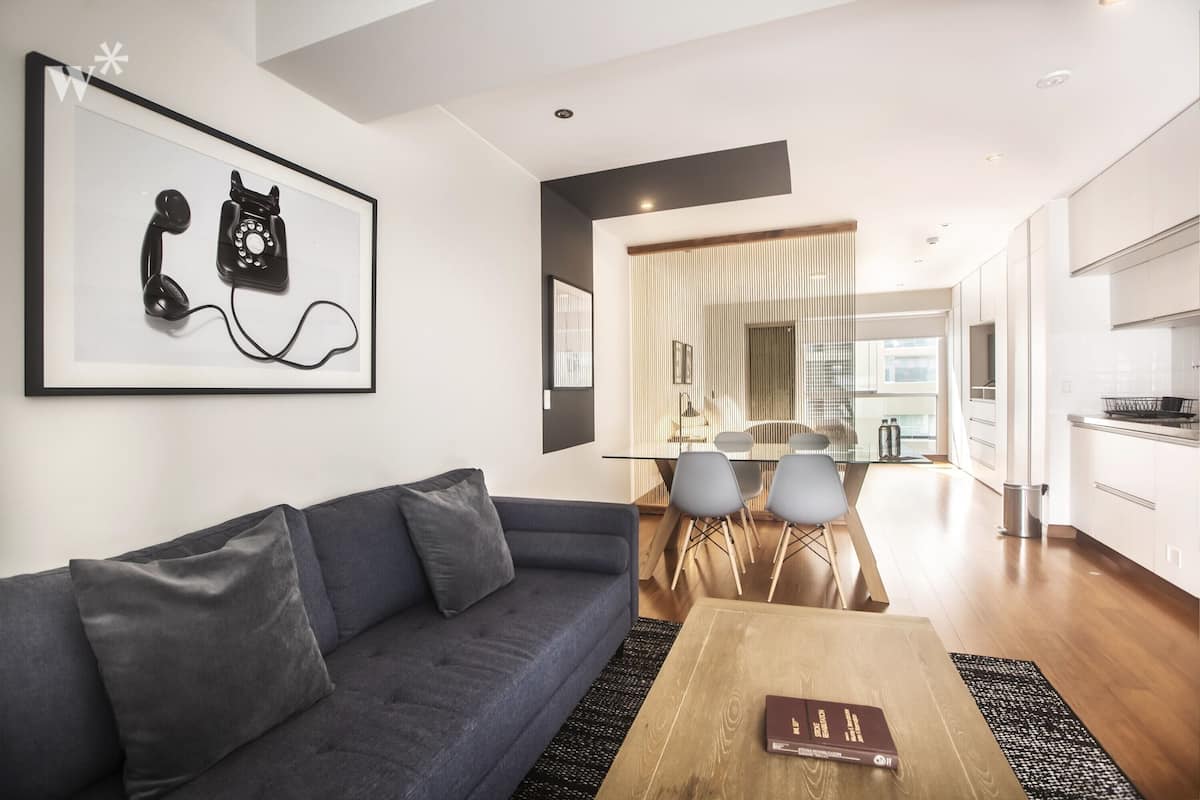 Ein modernes Wohnzimmer mit einer dunklen Couch, einem Holztisch und einem gerahmten Kunstwerk im Stil eines Telefons an der Wand.