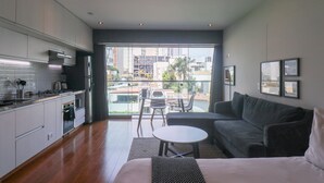 A modern kitchen with a dining area, a sofa, and a balcony with a view of buildings and greenery. - Wynwood Las Mimosas in Barranco (Lima)