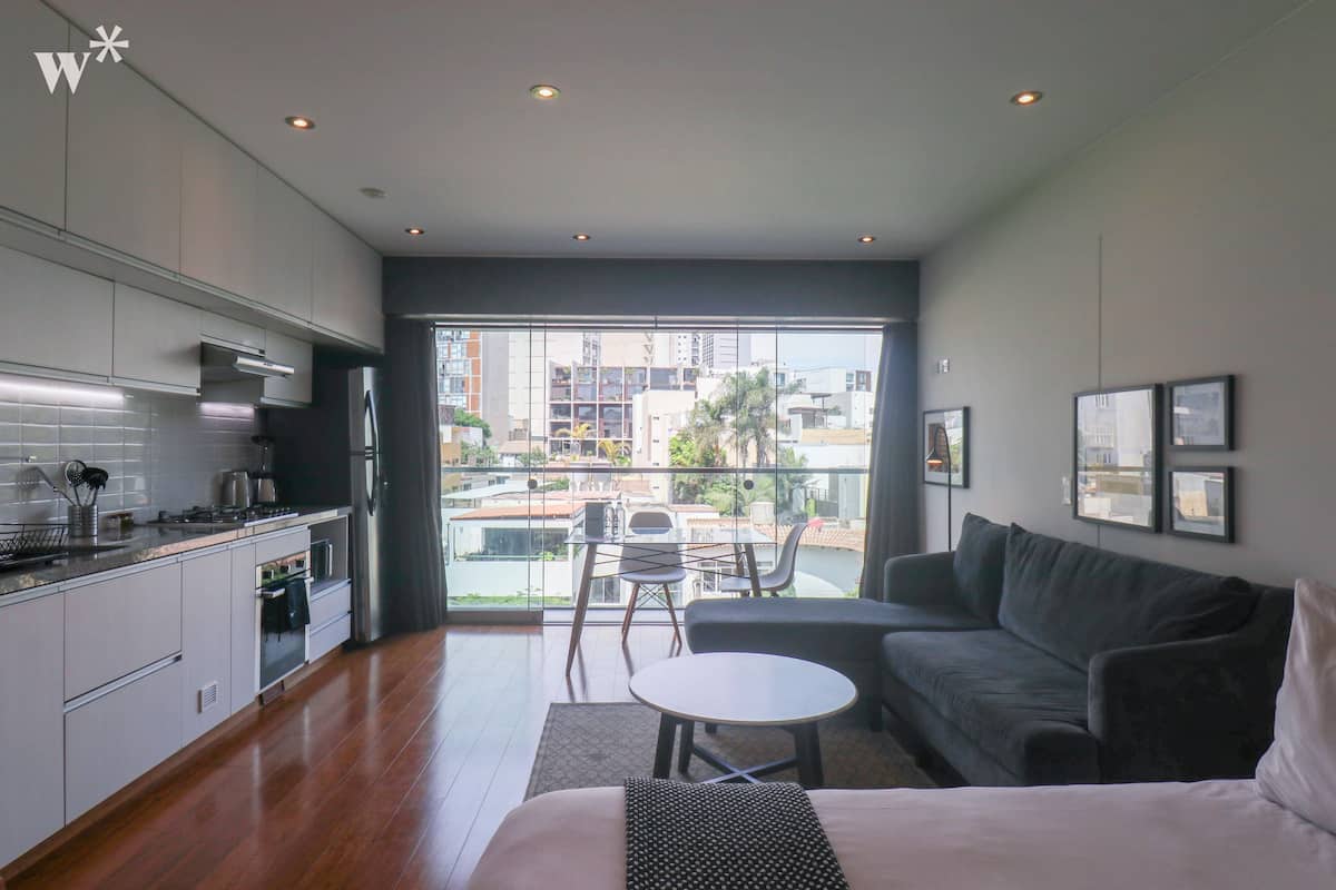 Eine moderne Küche mit Essbereich, einer Couch und einem Balkon mit Blick auf Gebäude und Grünflächen.
