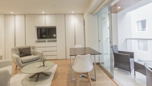 A modern living room with a sofa, a coffee table, and a dining table with chairs. There is a TV mounted on the wall and a balcony with wicker furniture. - Wynwood Las Mimosas in Barranco (Lima)