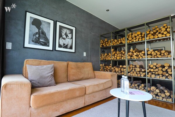 A living room with a beige sofa, two framed artworks, and a wooden log display.
