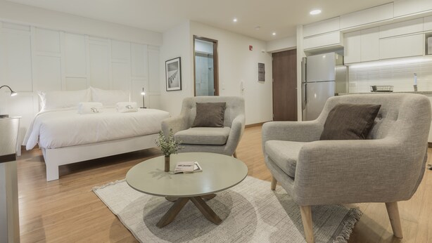 A modern hotel room with a bed, two armchairs, a coffee table, a small plant, and a kitchen area. - Wynwood Las Mimosas in Barranco (Lima)